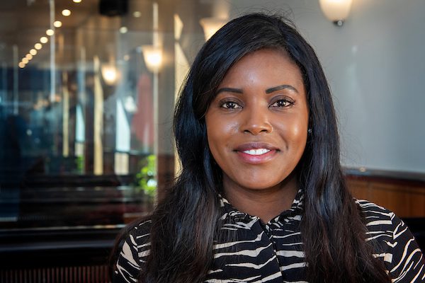 Portrait of Bayile Adeoti. Bayile, is a black female with long dark hair, and wearing a zebra print top.