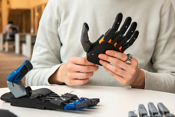 Close up image of founder holding one of the prosthetic hand designs, with two other designs on the table in front.