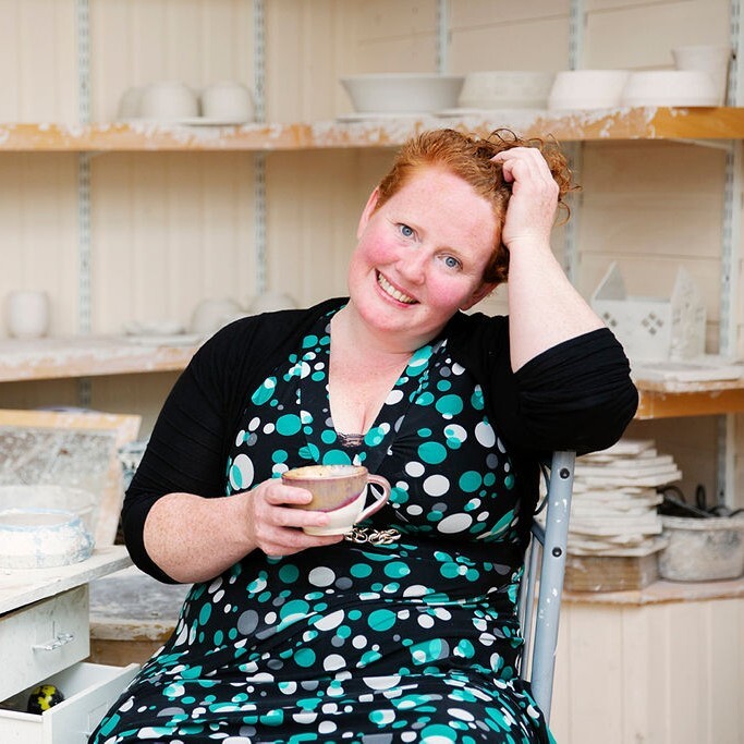 Image of Renae smiling at the camera with one hand in her hair and the other holding a mug