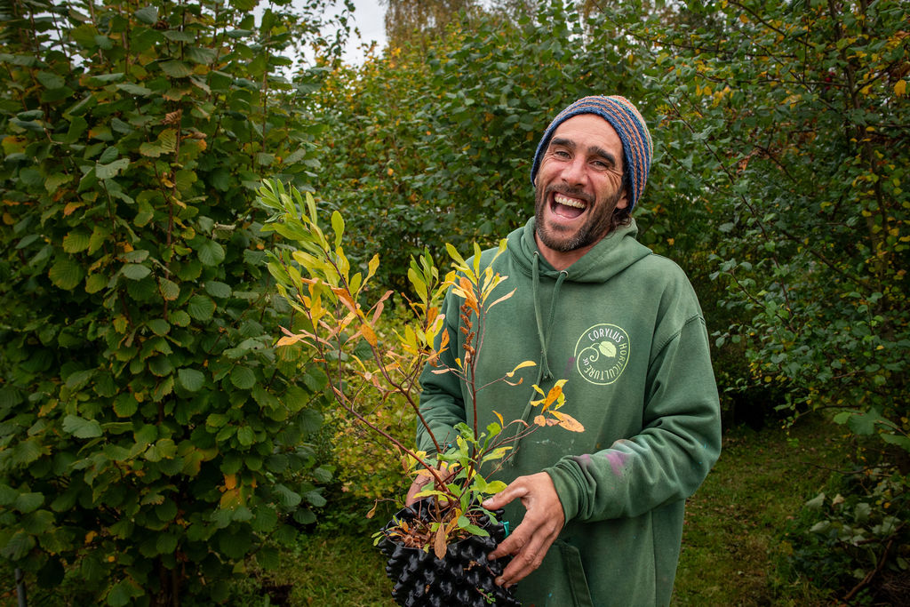 Image of Ed from Corylus Horticulture holding a plant and smiling at the camera