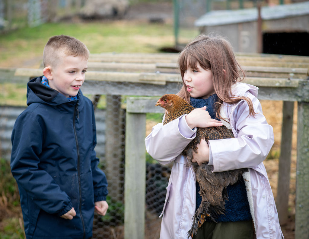 Two young people with a chicken at The Paddock Broom of Moy CIC