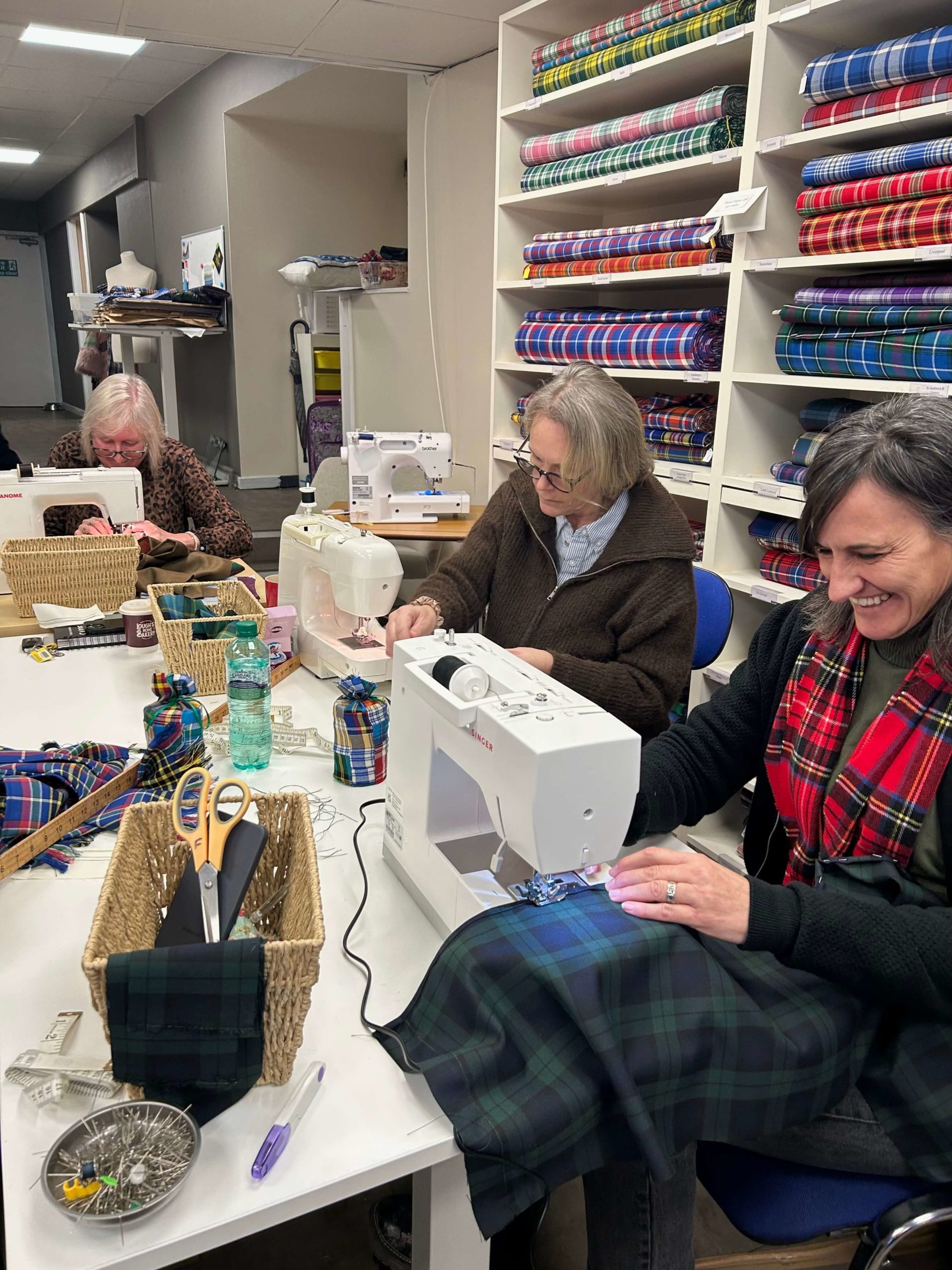Image of three people using sewing machines on tartan fabric