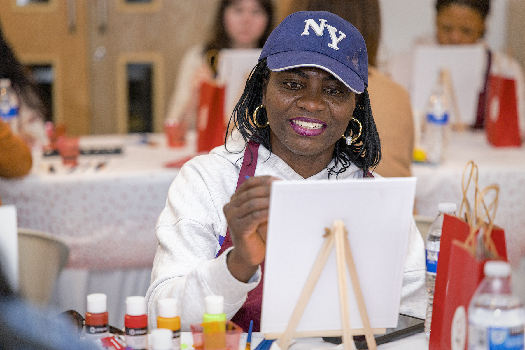 A person with a cap on smiles as they paint at an Adelphe Connect event.