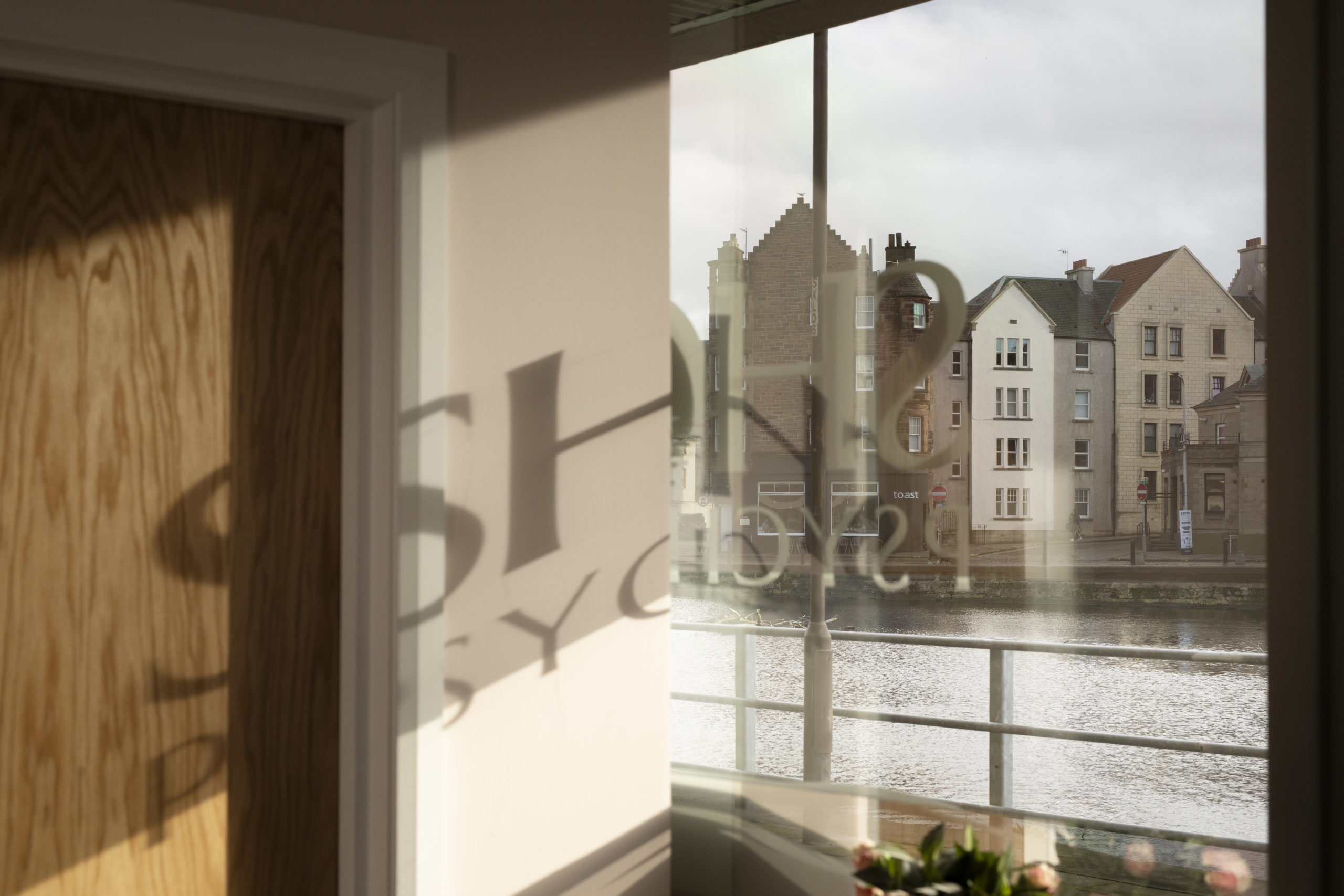 The window at Shore Psychology looking out at the Shore in Leith with the Shore Psychology logo reflected on the walls